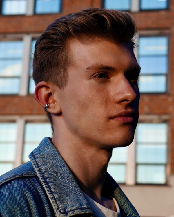 Sterling silver minimalist ear cuff worn by male model in denim jacket, urban background