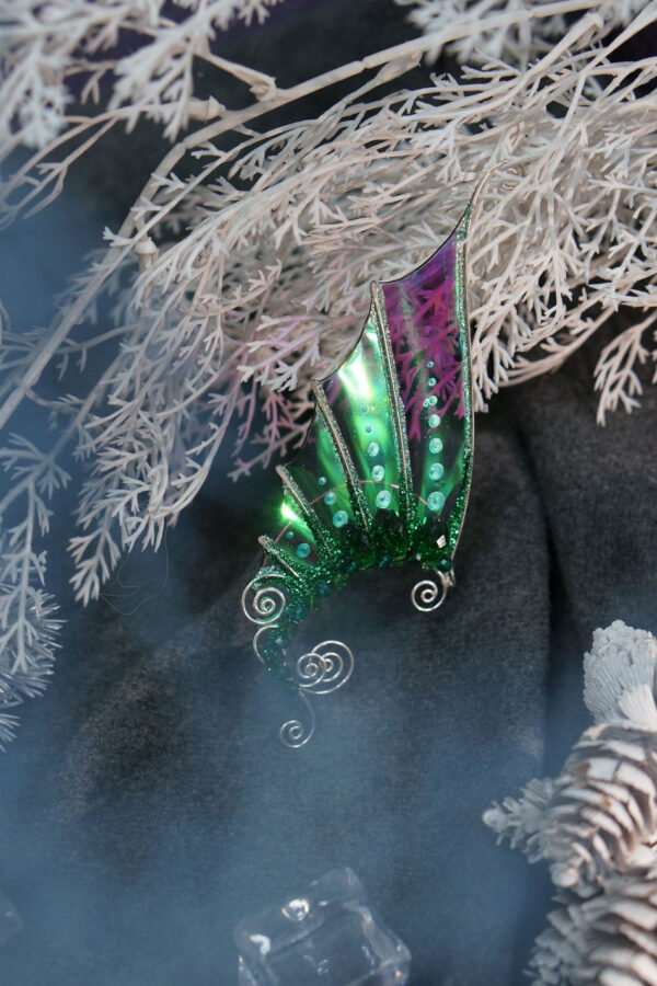 Handmade green mermaid ear cuff with glitter placed among frosty white branches and decorative elements