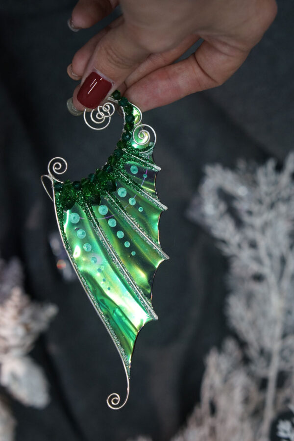 Hand holding a handmade green mermaid ear cuff with glitter on a dark background