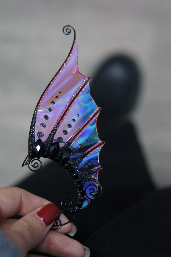 Hand holding a black handmade mermaid ear cuff with iridescent finish
