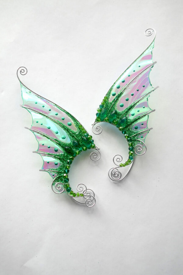 Pair of handmade green mermaid ear cuffs with glitter and beads on a white background