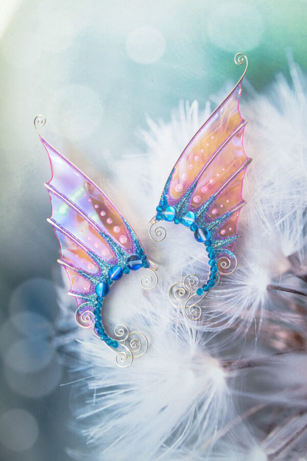 Pair of handmade pink and blue mermaid ear cuffs with glitter placed on dandelion fluff background