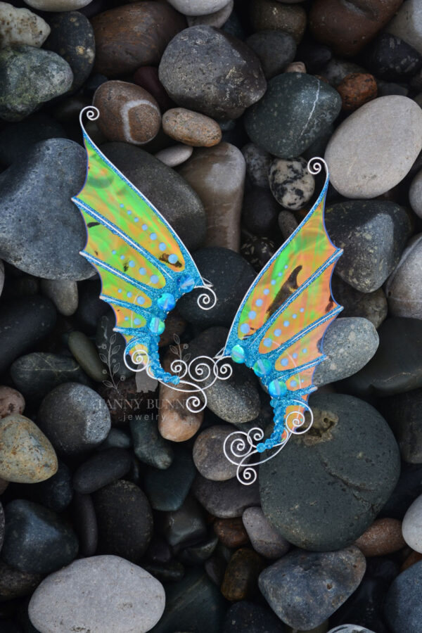 Pair of handmade gold and blue mermaid ear cuffs with glitter placed on sea stones