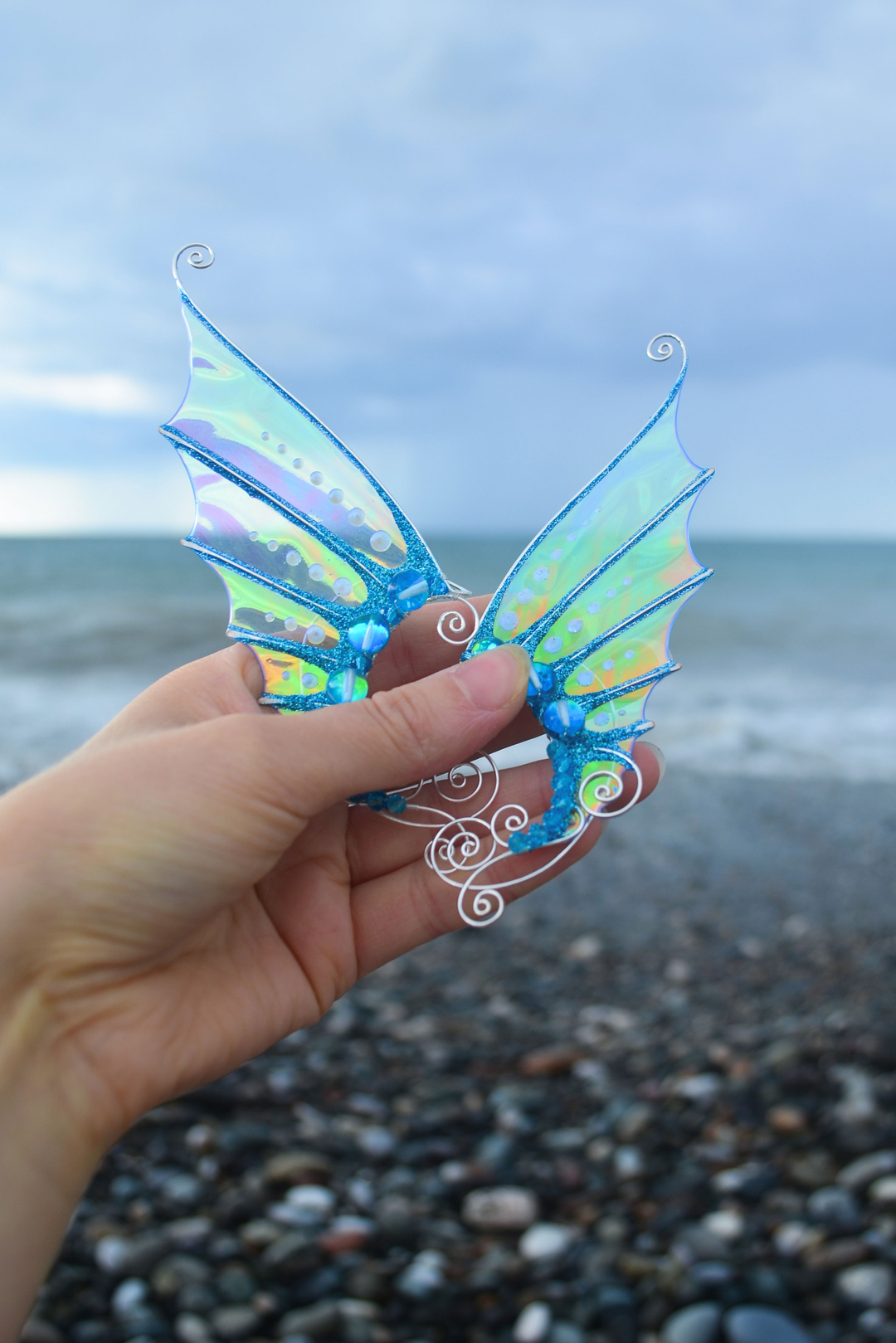 Golden and blue handmade mermaid ear cuffs held in hand by the sea, no piercing needed