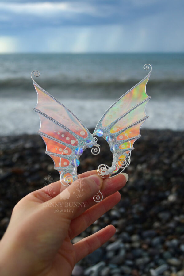Hand holding a pair of handmade gold mermaid ear cuffs with white glitter in front of the sea