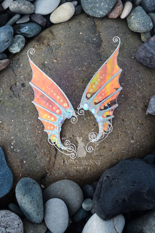 Handmade gold mermaid ear cuffs with white glitter placed on wet beach stones
