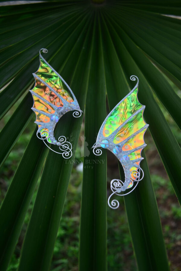 Pair of handmade gold mermaid ear cuffs with glitter displayed on tropical green leaves