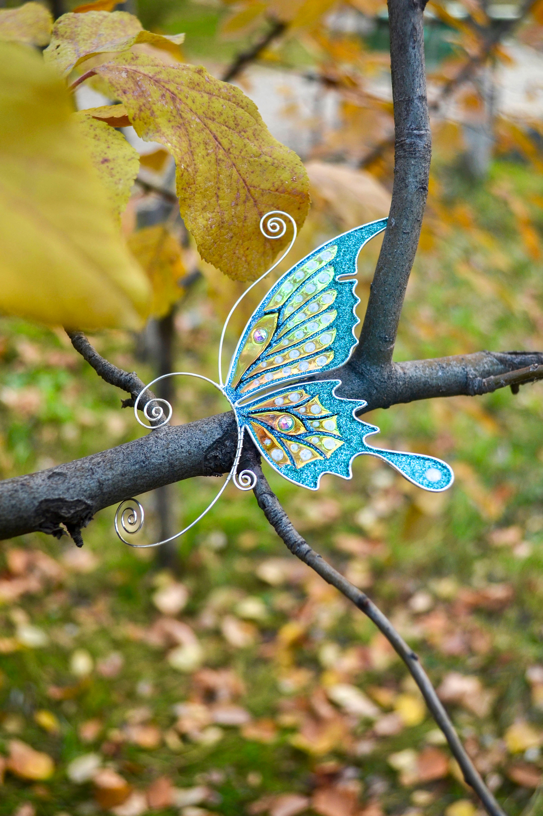 Teal and gold handmade butterfly ear cuff placed on a tree branch, fairy wing earring, no piercing needed