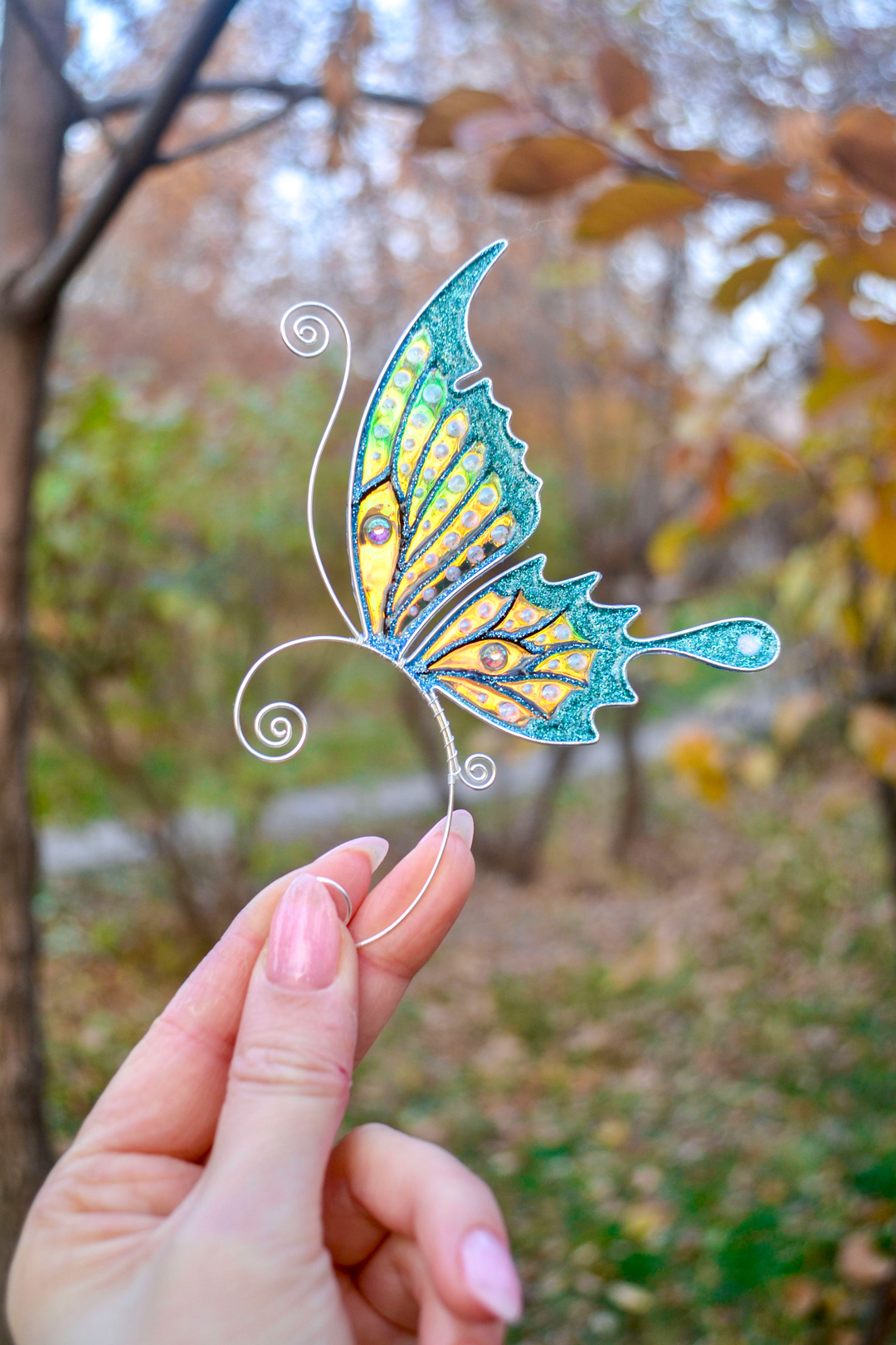 Handmade butterfly ear cuff held in hand outdoors, teal glitter fairy wing earring, no piercing needed