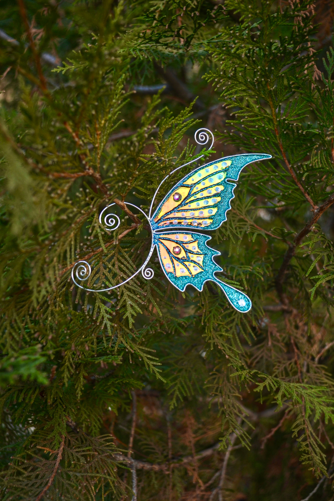 Teal and gold butterfly ear cuff on green conifer branches, handmade fairy wing earring