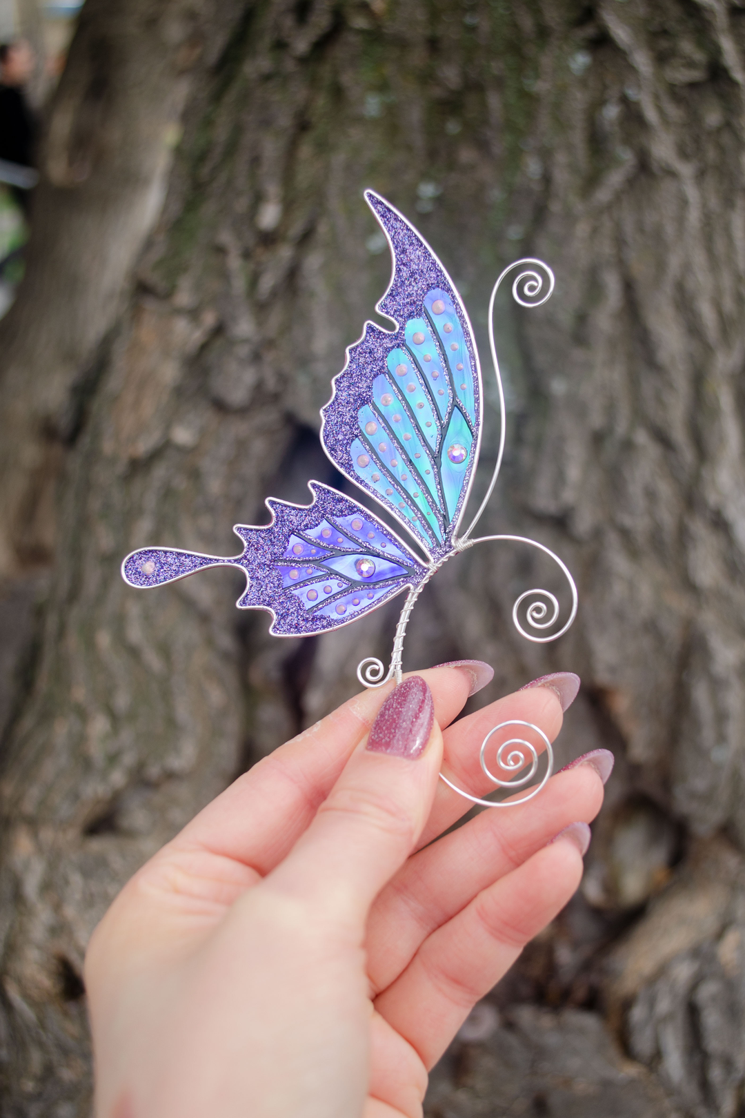 Purple handmade butterfly ear cuff held in hand against tree bark, fairy wing earring