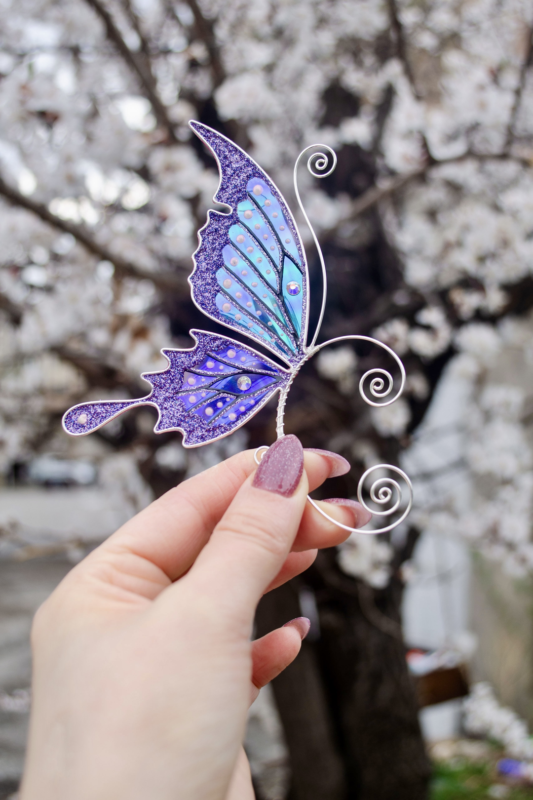 Purple handmade butterfly ear cuff held in hand with blooming tree background, fairy wing earring