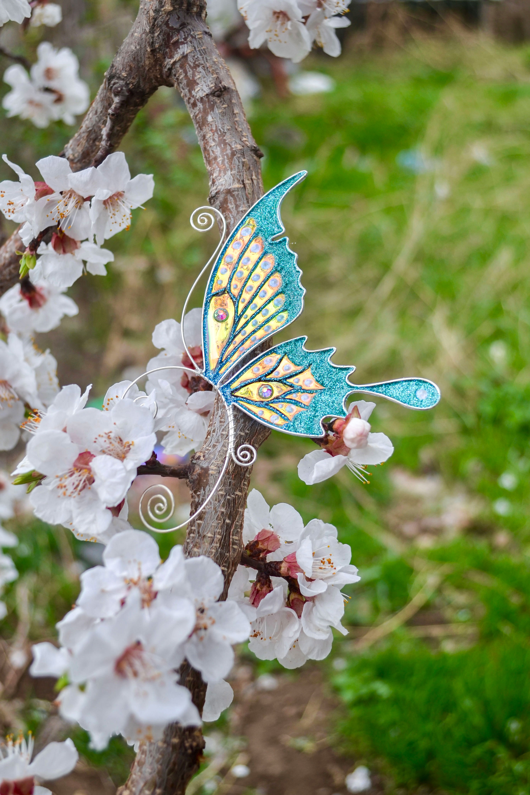 Butterfly ear cuff placed among blooming white flowers, handmade teal fairy wing earring