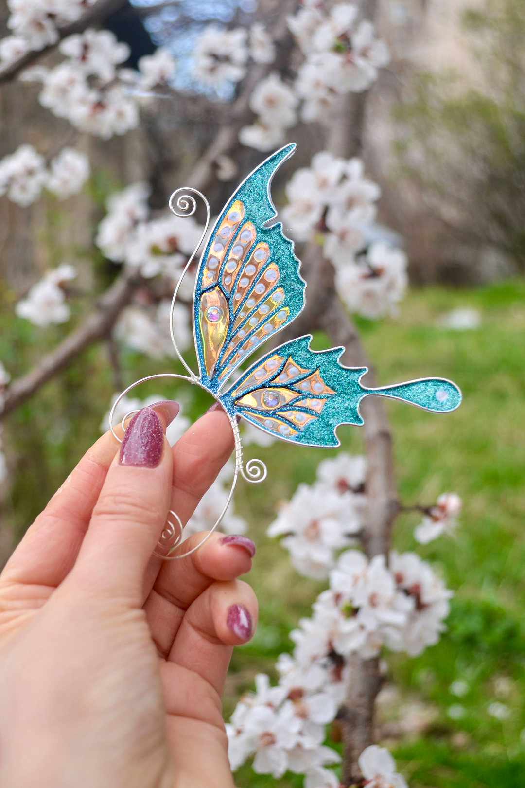 Handmade butterfly ear cuff held near spring blossoms, teal glitter fairy wing earring