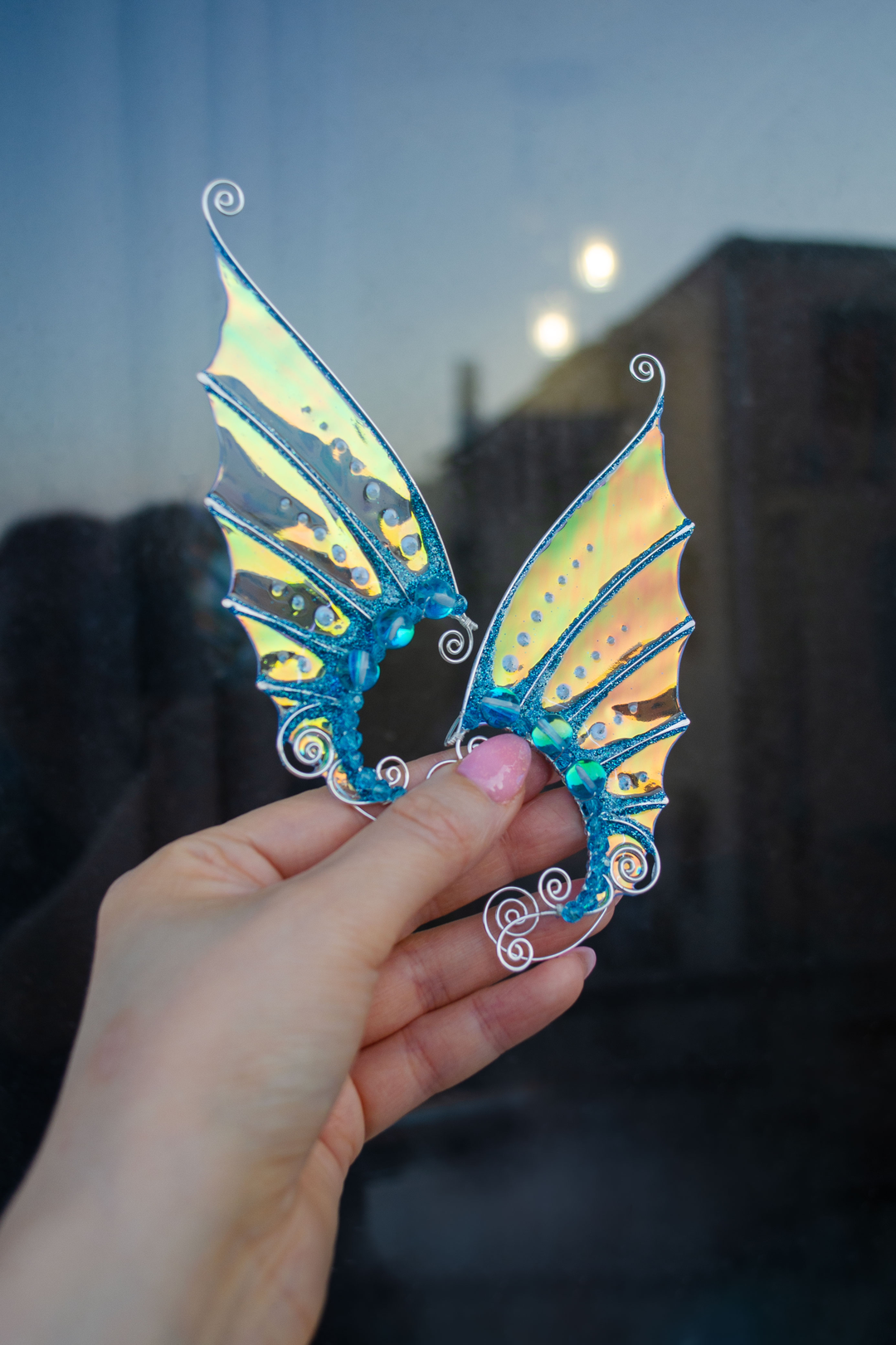 Golden and blue mermaid ear cuffs held in hand with evening city reflection, handmade cosplay earrings