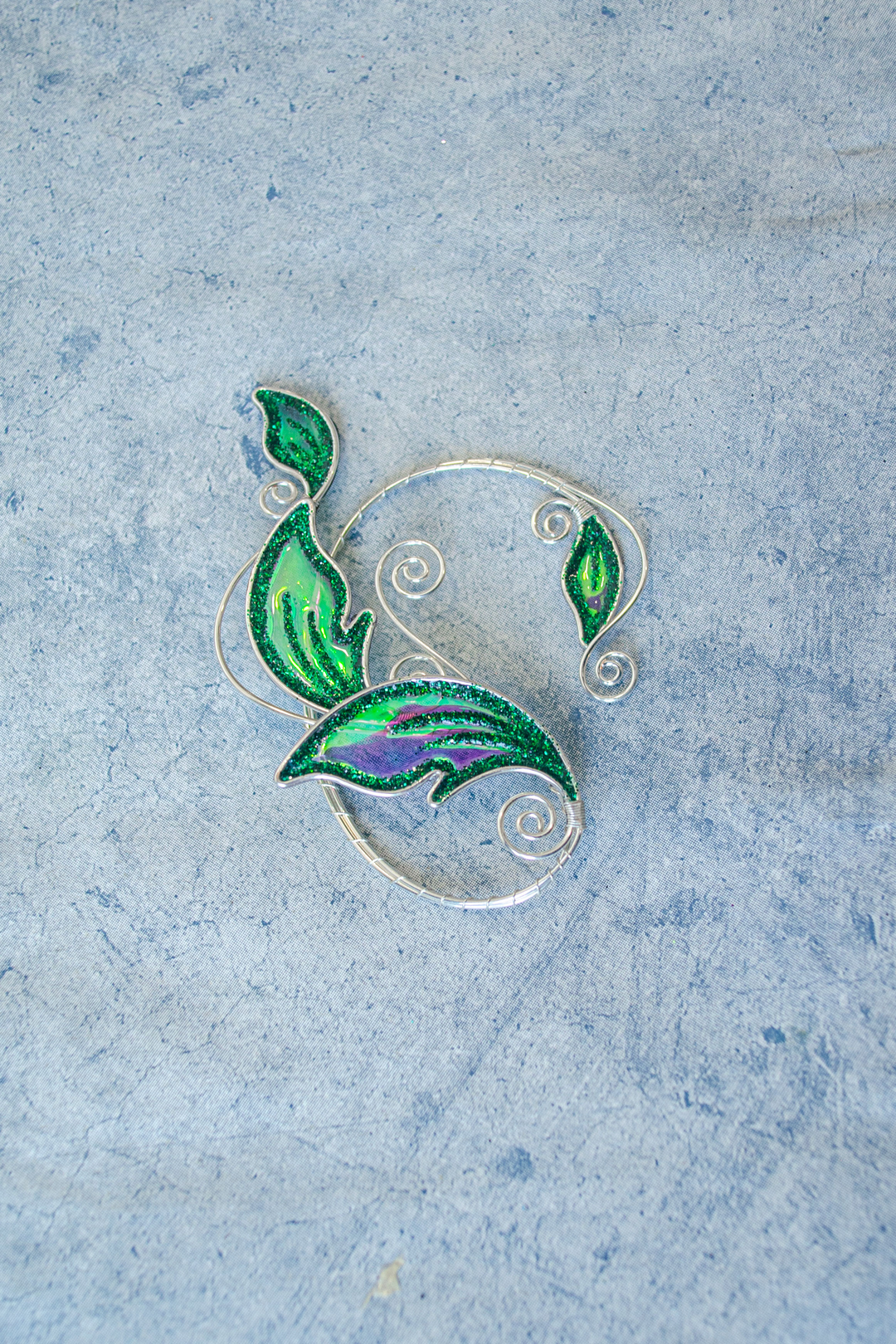 Emerald green handmade elven leaf ear cuff on blue textured background