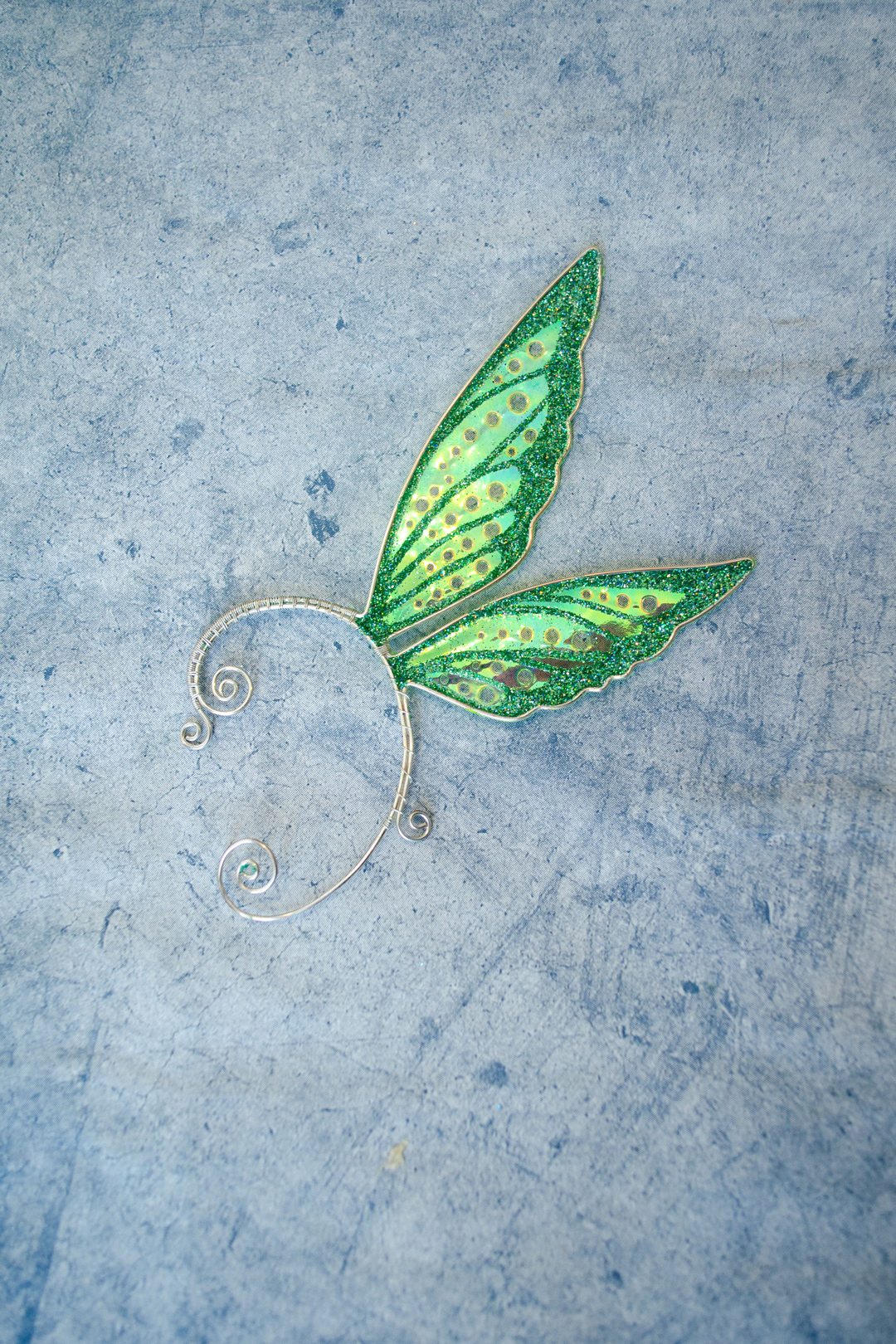 Fairy cosplay ear cuff, green, handmade, no piercing needed, fairy earring — green fairy wing cuff lying on textured grey stone background.