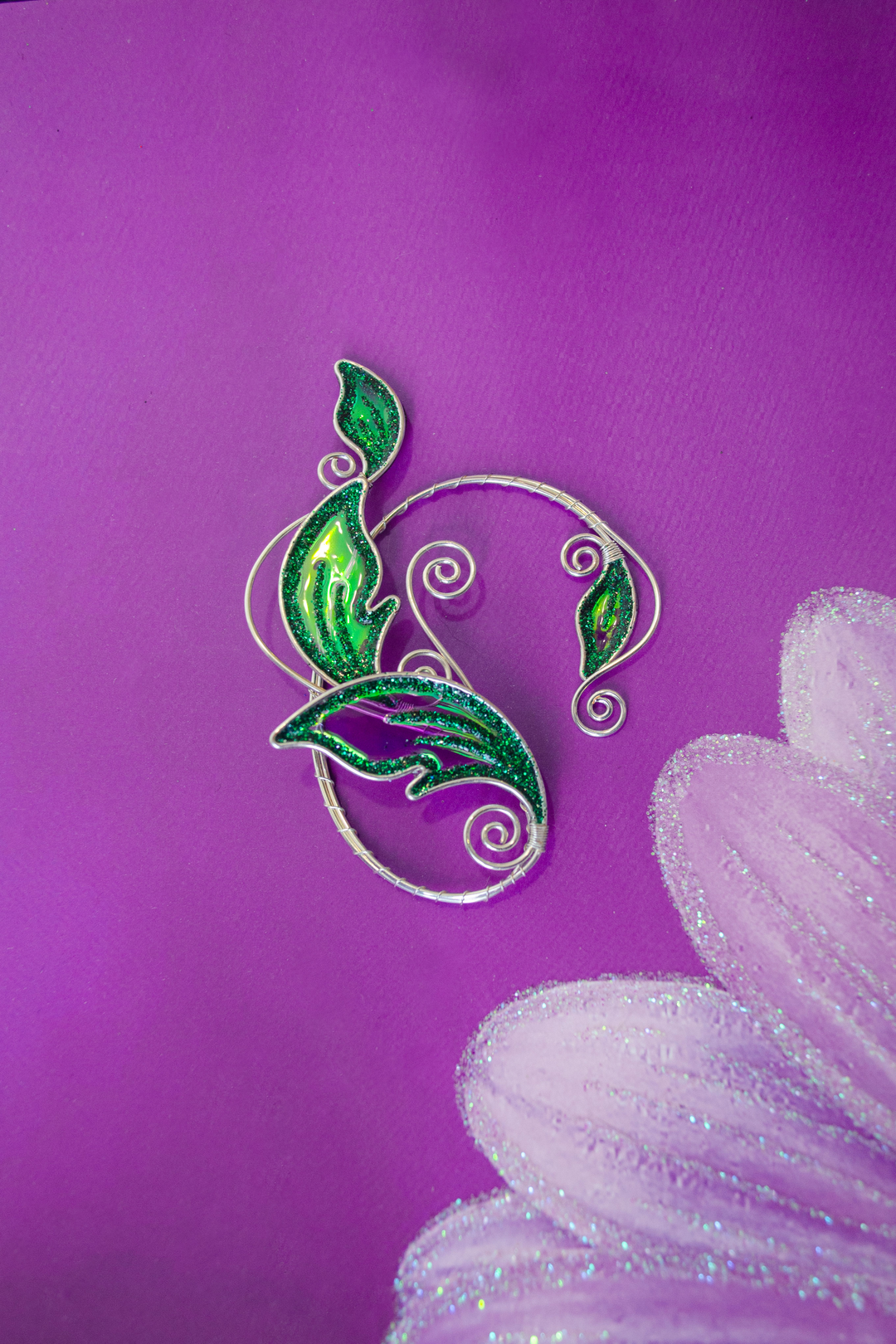 Emerald green elven leaf ear cuff on purple painted background, handmade fantasy ear cuff