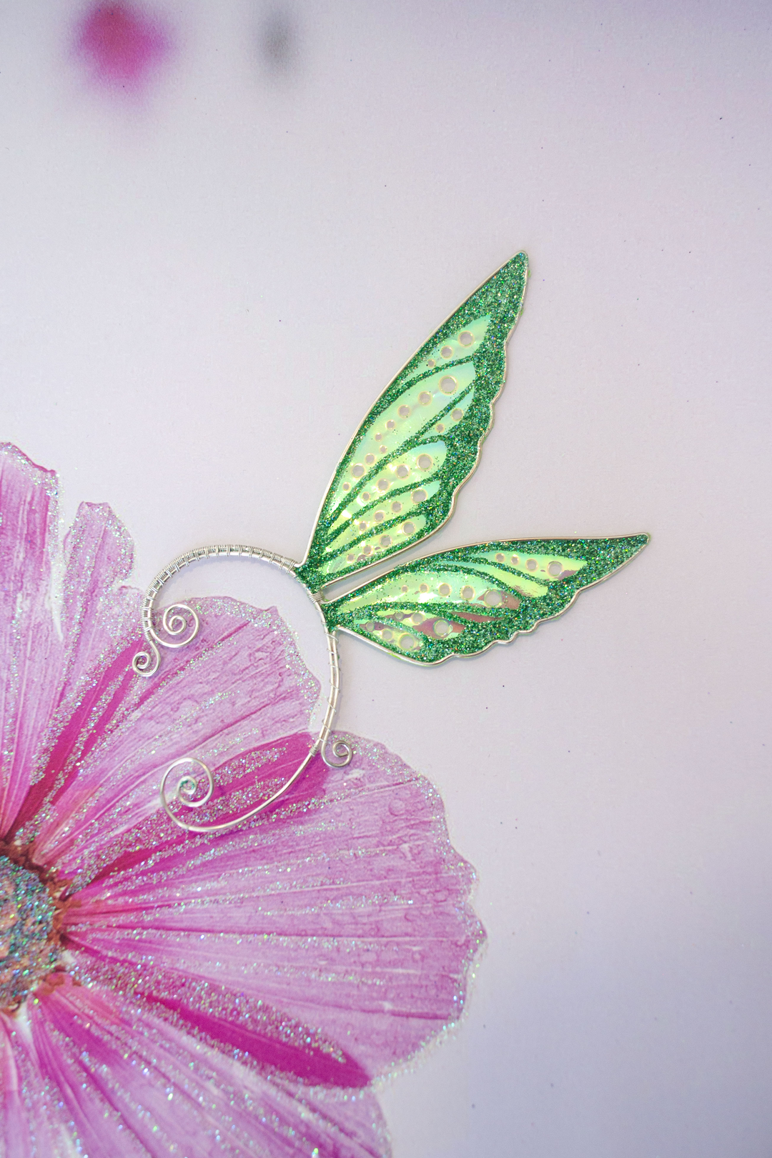 Fairy cosplay ear cuff, green, handmade, no piercing needed, fairy earring — green wing ear cuff placed on pink flower illustration.