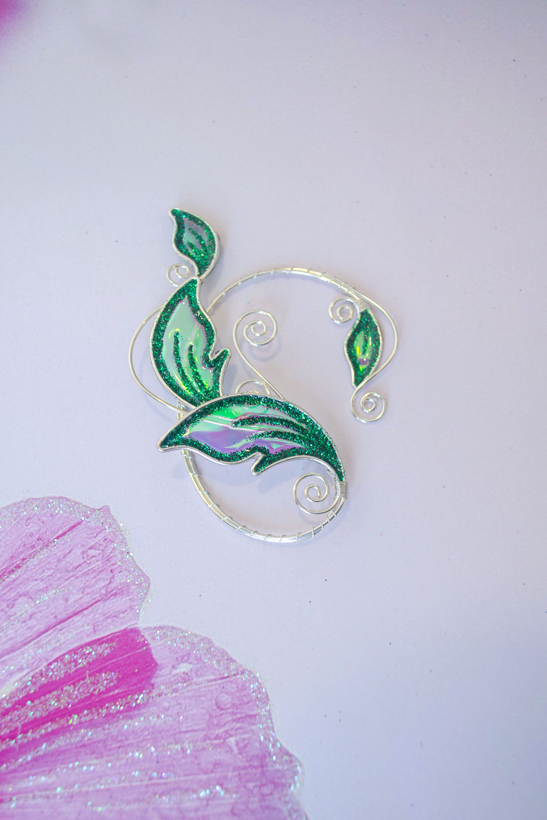Emerald green handmade elven leaf ear cuff on pastel pink background with painted petals