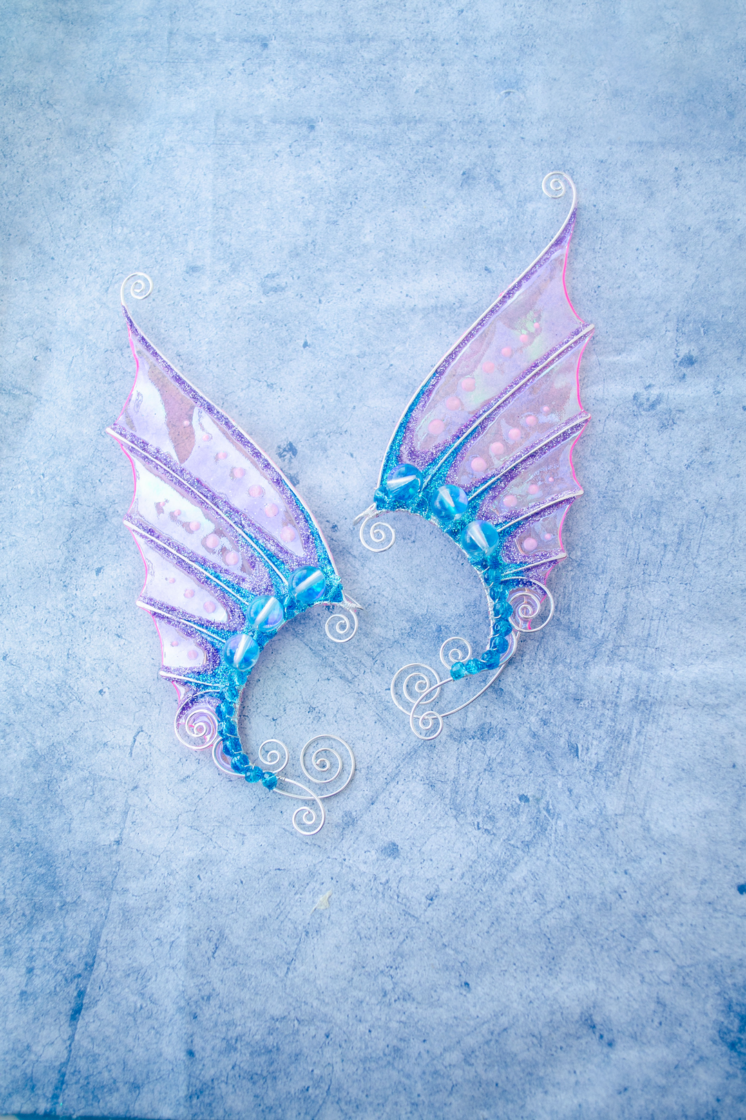 Pair of handmade pink and blue mermaid ear cuffs on a textured blue background