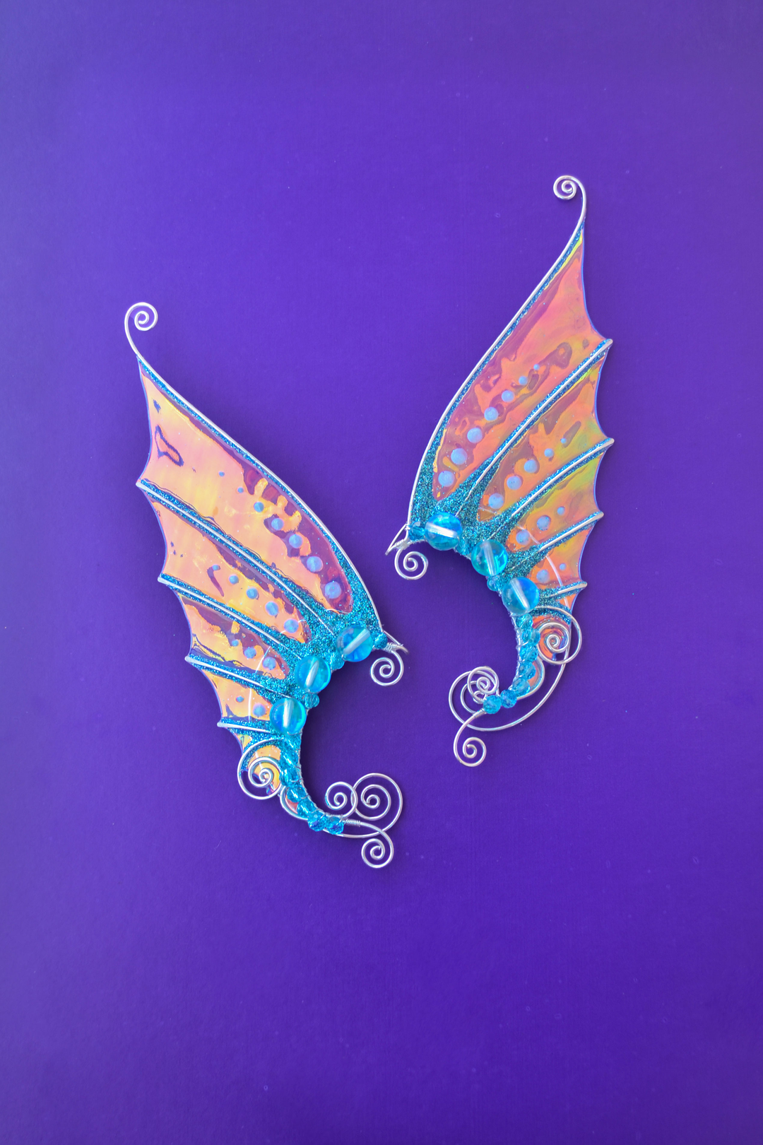 Golden and blue handmade mermaid ear cuffs on purple background, no piercing needed