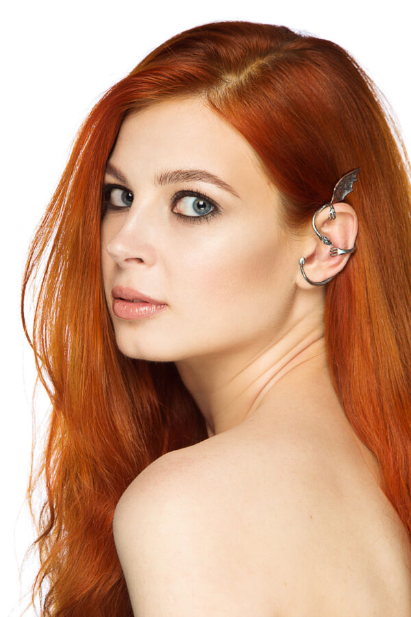 Sterling silver dragon ear cuff with wing and curled tail, worn on left ear by red-haired woman with loose hair