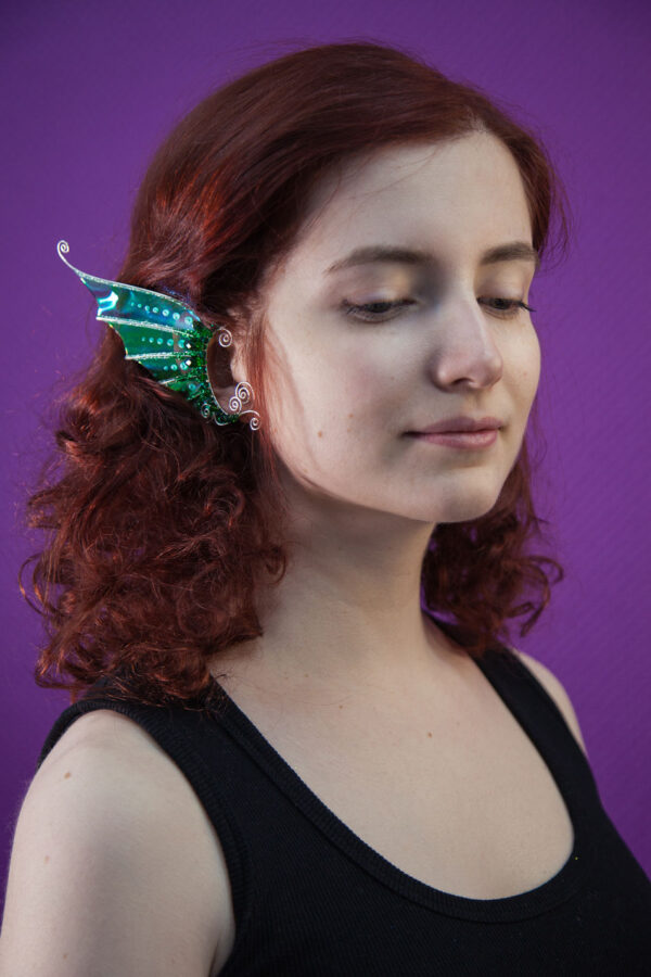 Model with curly red hair wearing a handmade green mermaid ear cuff with glitter on a purple background