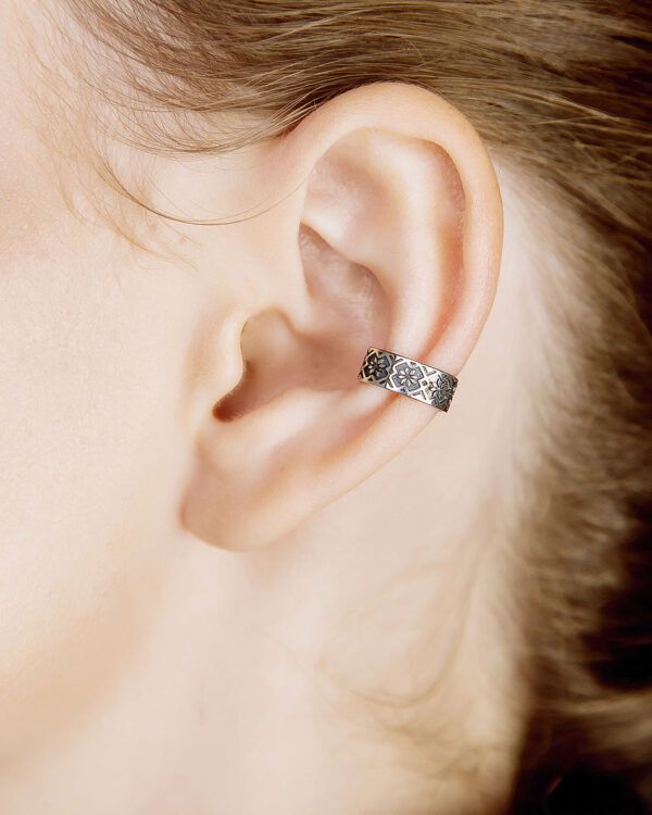 Silver Slavic ear cuff with ethnic pattern worn on ear, adjustable oval design