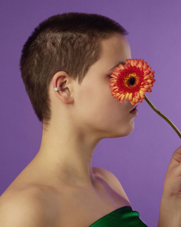 Silver ear cuff with stones worn by model with buzz cut holding a red flower