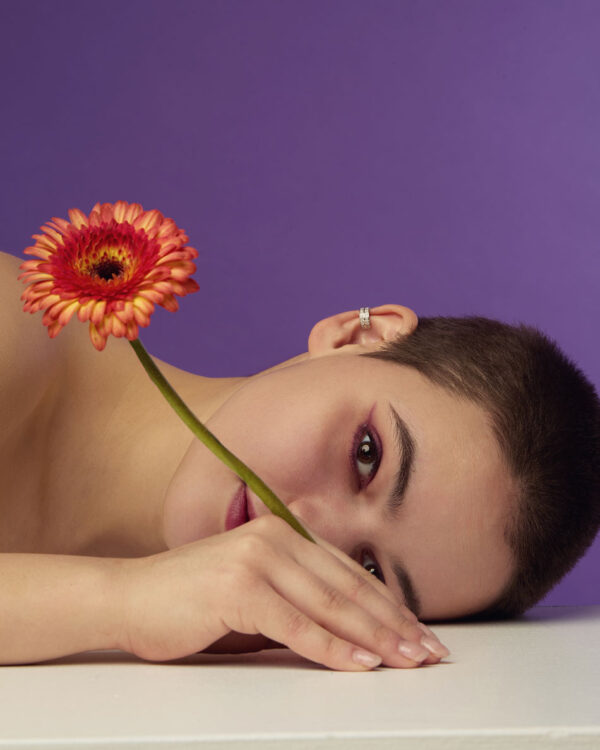 Silver ear cuff with stones worn by model lying on table, flower in foreground