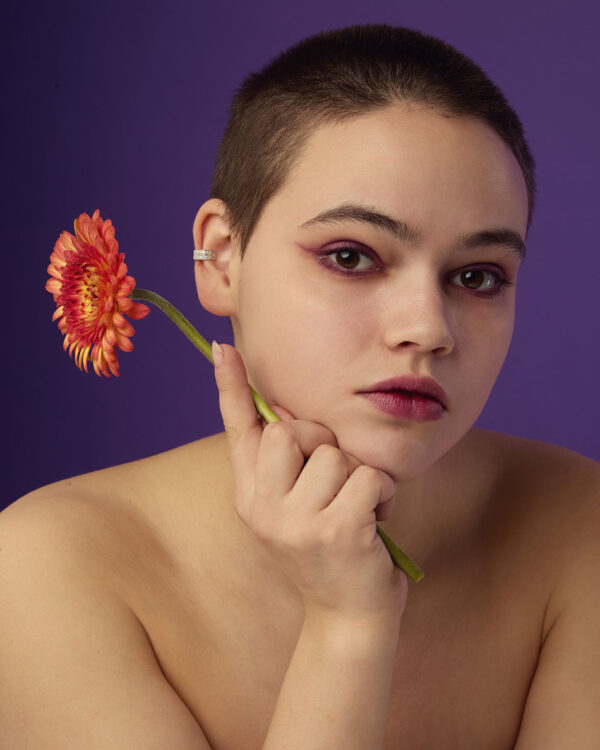 Model with short hair wearing silver ear cuff with stones, holding orange flower