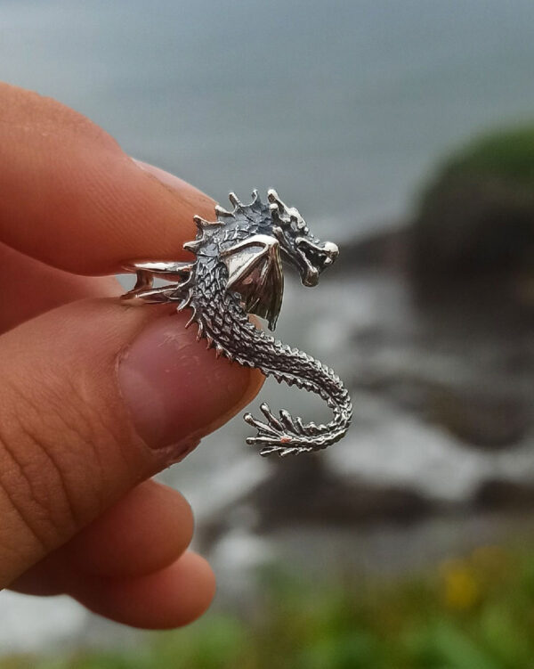 Hand holding silver dragon ear cuff against ocean background