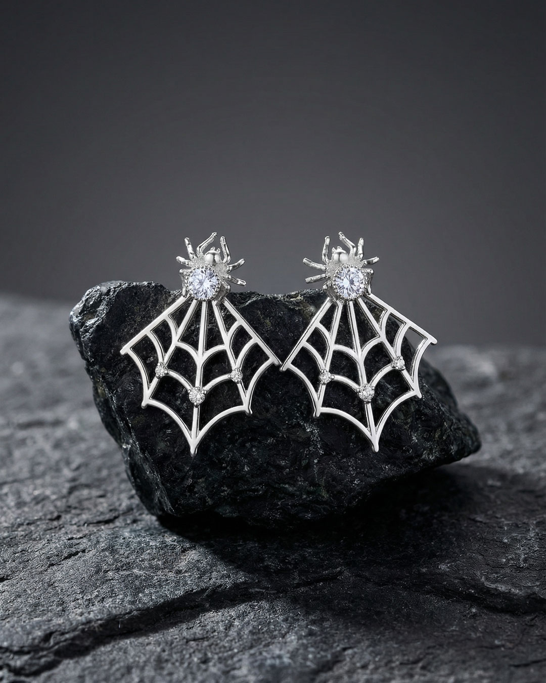 spider web ear jacket earrings displayed on dark stone surface