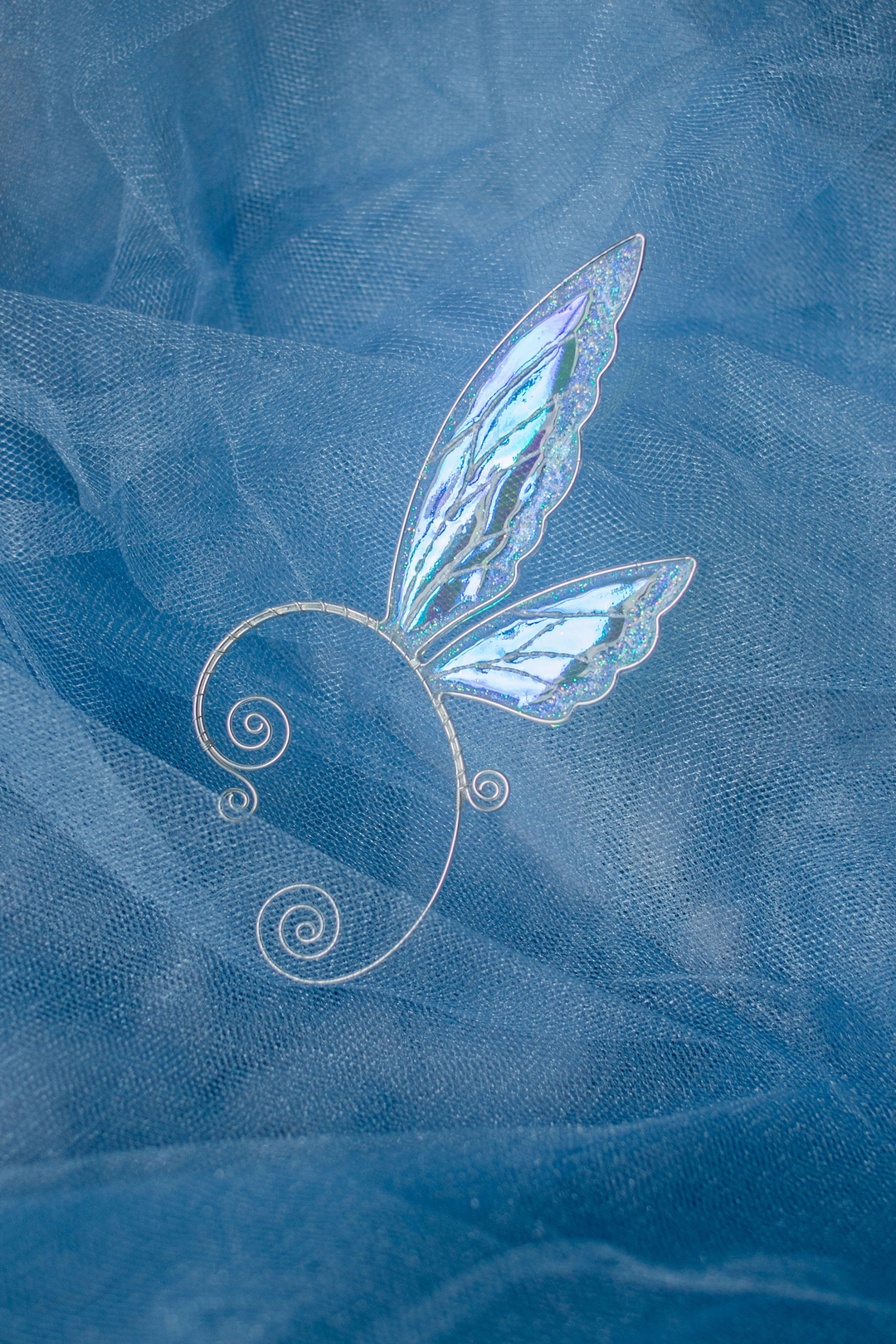 fairy wing ear cuff in white iridescent design on blue textile background