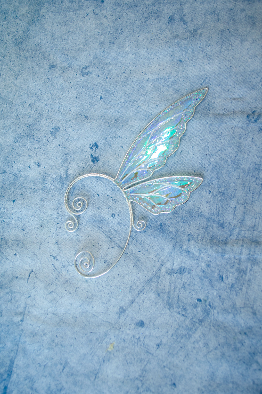 fairy wing ear cuff in white iridescent design placed on textured stone background