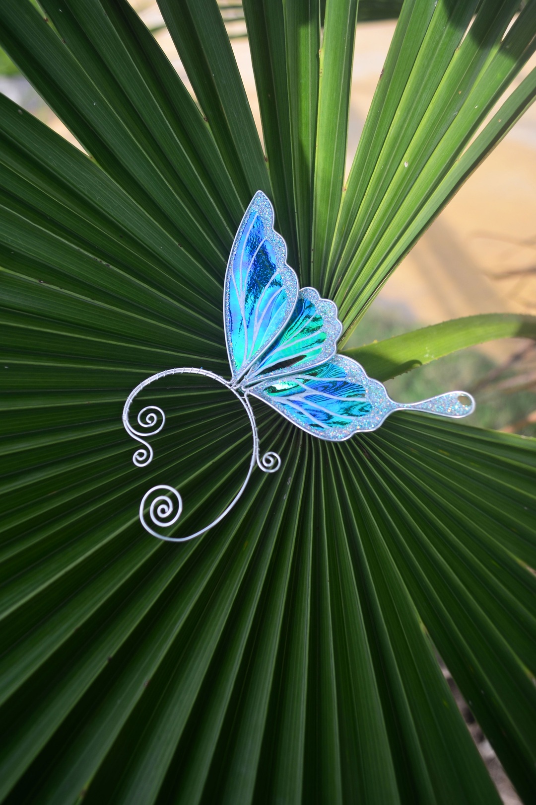 iridescent fairy wing ear cuff in green and white on palm leaf, handmade no-piercing jewelry
