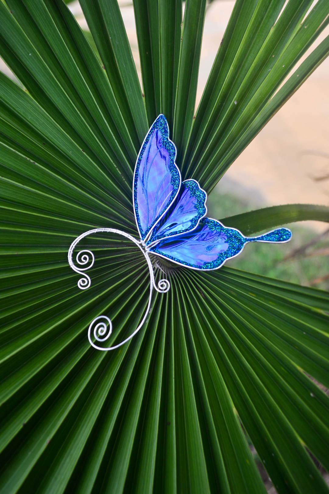 Iridescent blue fairy wing ear cuff on a green palm leaf, handmade wire design