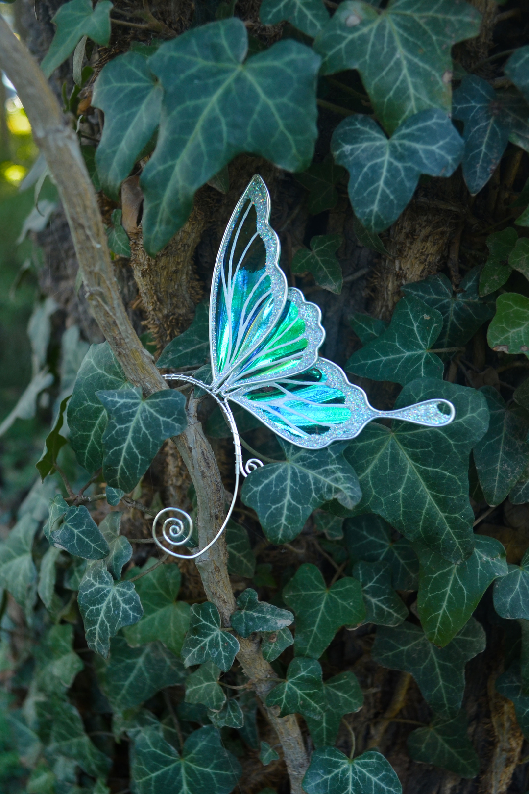 iridescent fairy wing ear cuff in green and white displayed on ivy, handmade fairy cosplay jewelry