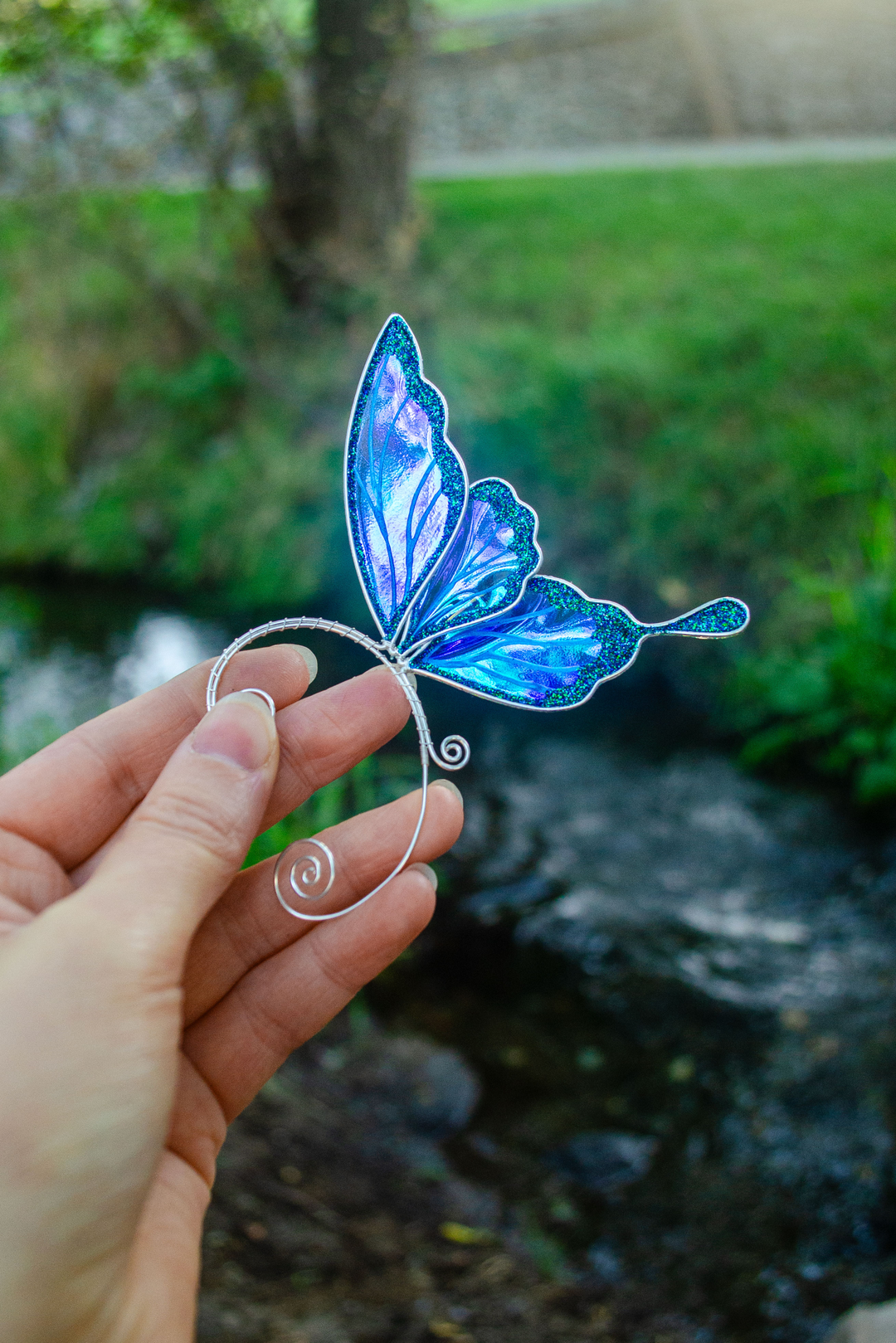 Hand holding iridescent blue fairy wing ear cuff outdoors