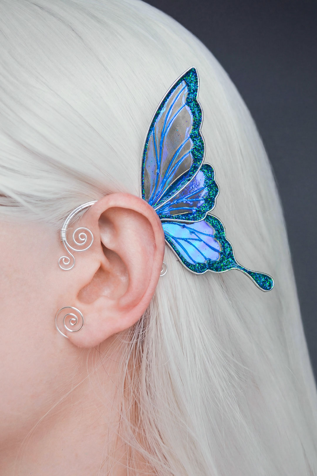 Iridescent blue fairy wing ear cuff worn on ear, close-up, no piercing