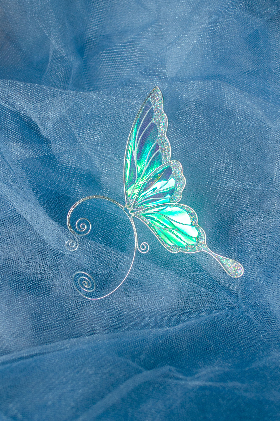 iridescent fairy wing ear cuff in green and white on soft blue fabric background