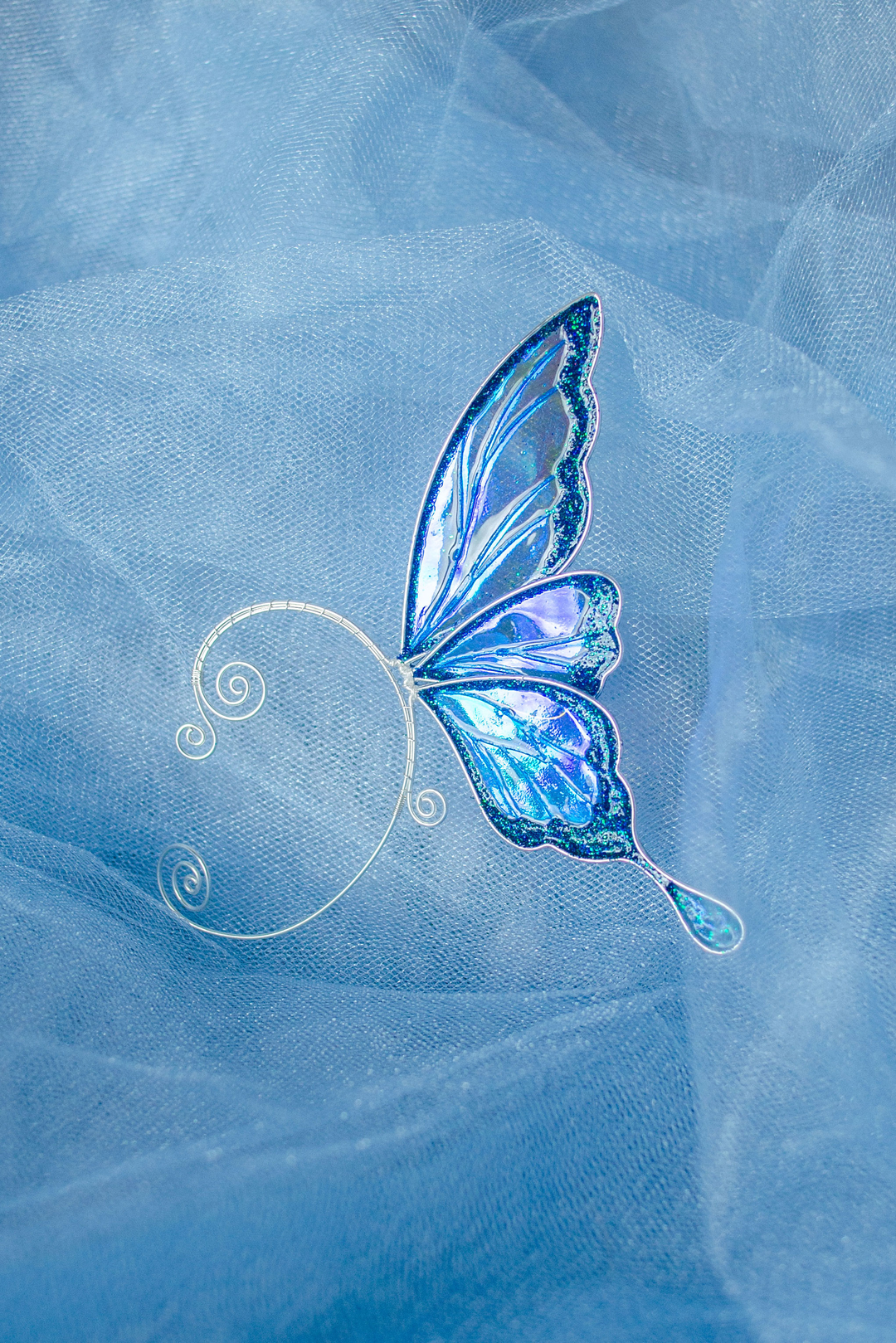 Iridescent blue fairy wing ear cuff on soft blue fabric background
