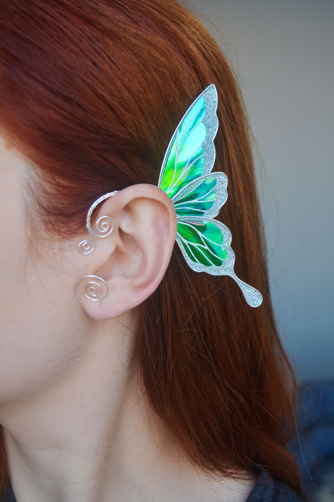iridescent fairy wing ear cuff in green and white worn on ear, handmade no-piercing fairy cosplay earring