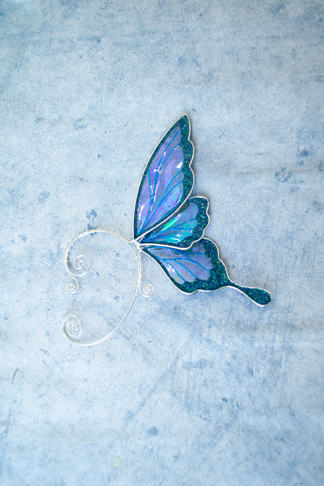 Blue iridescent fairy wing ear cuff on light blue textured background