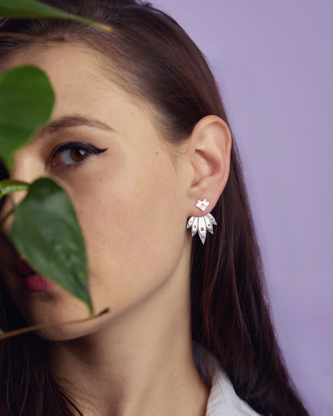 Fox ear jacket earrings on model partially covered by leaves