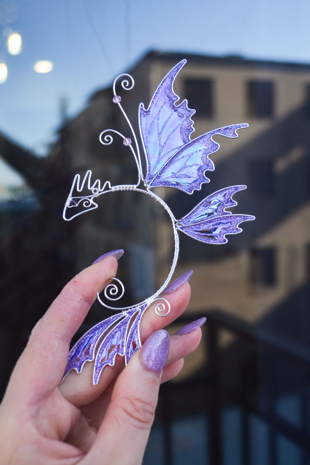 fairy dragon ear cuff held in hand, handmade fairy cosplay jewelry in urban setting