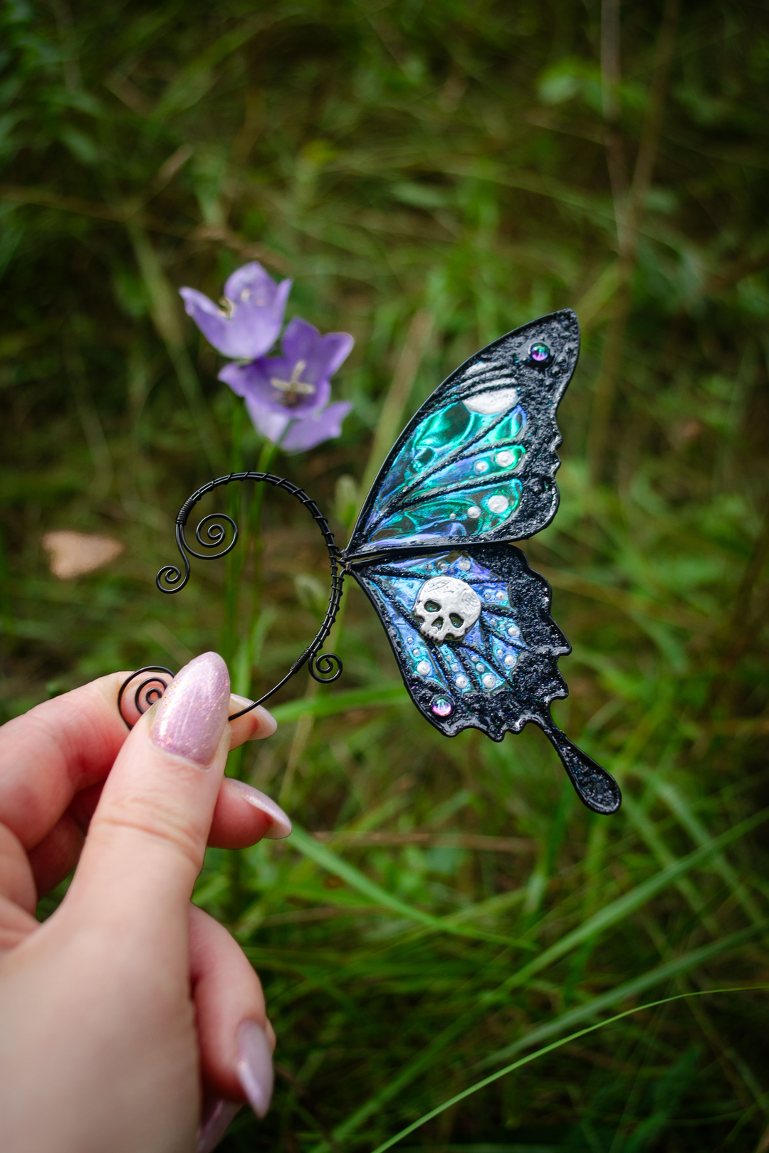 Gothic butterfly ear cuff with skull held near purple flowers