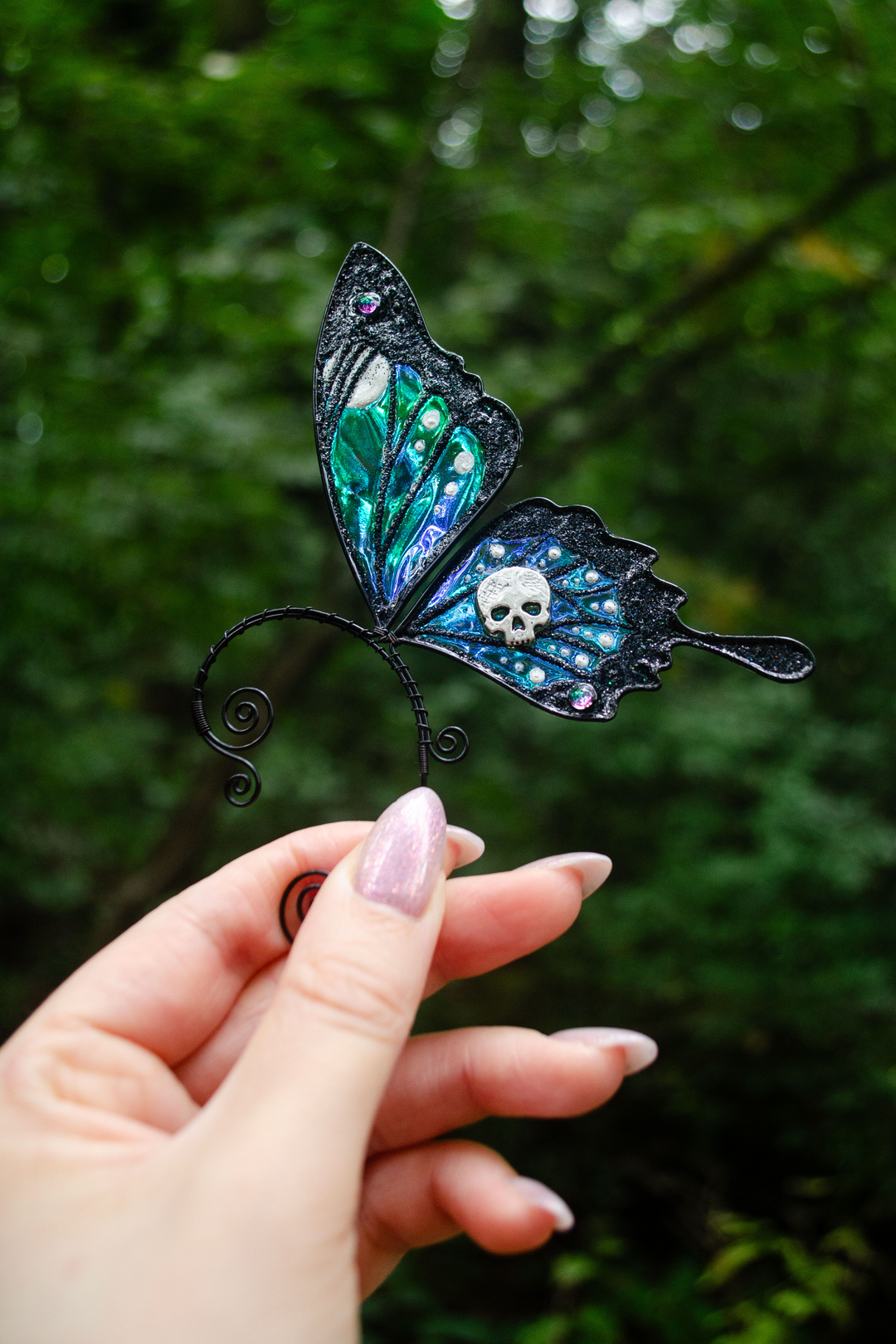 Gothic butterfly ear cuff with skull held among green leaves