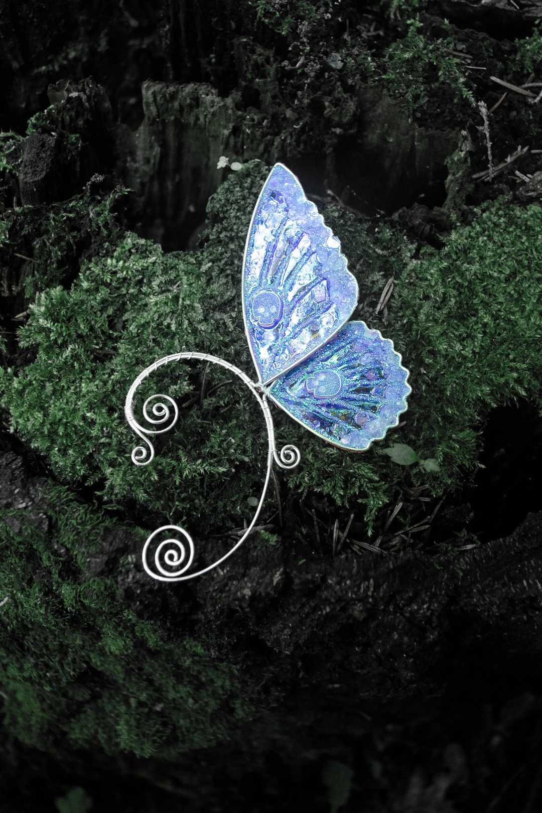 Blue butterfly ear cuff with skull close-up on moss
